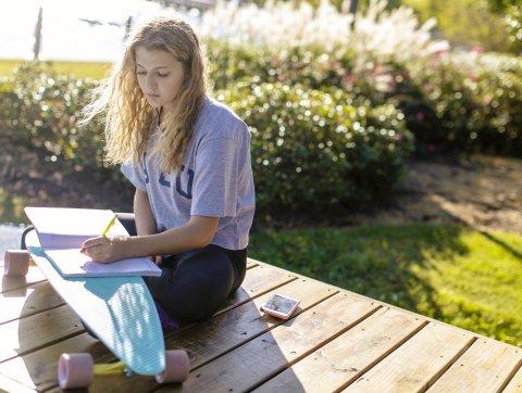 Student sits outside writing on notebook